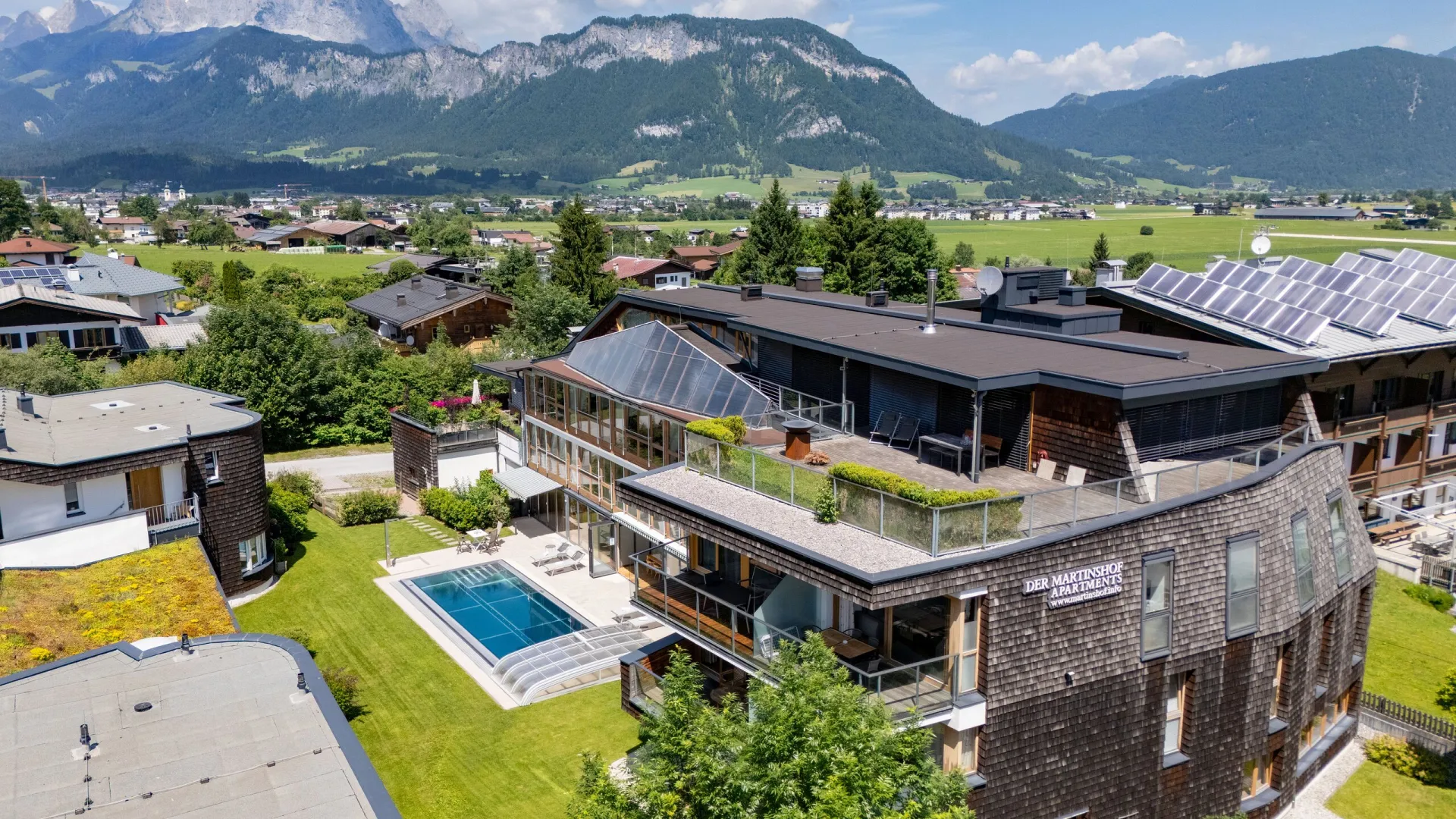 Luftaufnahme des Martinshofs mit Pool, dahinter der Wilde Kaiser